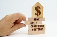 Real estate and business. On wooden blocks with the inscription - Home Equity Conversion Mortgage, there is a model of a house with a dollar symbol. The man's hand takes out the block.