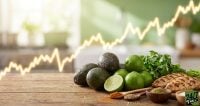 Fresh avocados, limes, and grilled chicken on a wooden table with a glowing yellow stock market line trending upwards in the background.