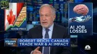 A financial news screengrab shows Robert Reich, an older man with gray hair and a beard, wearing a suit and tie, speaking. To his left, a graphic depicts the Canadian flag alongside a stack of lumber with an upward green arrow and the text 'HOUSE PRICE.' To his right, another graphic shows a human brain being held by a robotic hand, with the text 'AI JOB LOSSES.' A lower third banner across the screen reads 'ROBERT REICH: CANADA TRADE WAR & AI IMPACT.'