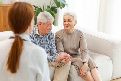 Female doctor examining older senior couple in doctor office or at home. Old woman man patient and doctor have consultation in hospital room. Medicine healthcare medical checkup. Visit to doctor