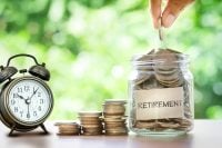 Hand putting Coins in glass jar for with retro alarm clock for time to money saving for retirement concept