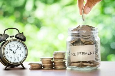Hand putting Coins in glass jar for with retro alarm clock for time to money saving for retirement concept