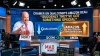 Jim Cramer, a man in a light blue shirt and red tie, smiles and points forward in a television studio. Behind him, a large screen displays the headline "CRAMER ON QUALCOMM'S AMAZON DEAL: 'SUDDENLY THEY'VE GOT SOMETHING SPECIAL'". The screen also shows Qualcomm and Amazon logos alongside text indicating "AMAZON AI DATA CENTER INFRASTRUCTURE" with an upward arrow. Below this, QCOM is shown with +3.17%. Studio cameras and additional monitors displaying stock charts are visible in the foreground.