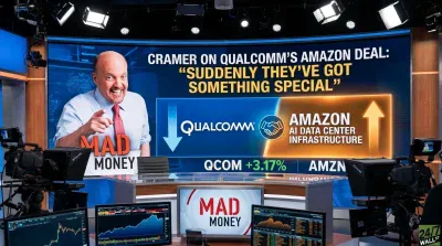 Jim Cramer, a man in a light blue shirt and red tie, smiles and points forward in a television studio. Behind him, a large screen displays the headline "CRAMER ON QUALCOMM'S AMAZON DEAL: 'SUDDENLY THEY'VE GOT SOMETHING SPECIAL'". The screen also shows Qualcomm and Amazon logos alongside text indicating "AMAZON AI DATA CENTER INFRASTRUCTURE" with an upward arrow. Below this, QCOM is shown with +3.17%. Studio cameras and additional monitors displaying stock charts are visible in the foreground.