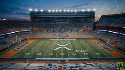 An aerial, wide shot of a college football stadium at dusk, with empty orange and blue seats. The green turf displays 'XRP' at midfield and 'ripple' near the 30-yard line, along with 'GATORA' and 'FLORIDA' in blue lettering on orange end zones. Financial candlestick charts and network connectivity lines are subtly overlaid across the image, which is illuminated by stadium lights.