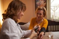 Happy senior Caucasian woman having blood pressure test performed by a mid adult doctor during house call visit and medical examination