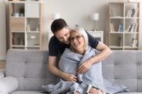 Let me take care of you. Caring attentive grown up millennial man son wrapping shoulders of grateful mom sit resting on sofa with warm woolen blanket protect loved parent from cold at cool living room