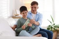 Dad giving his son pocket money on sofa at home