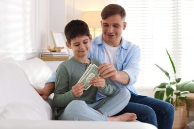 Dad giving his son pocket money on sofa at home