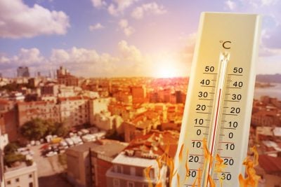 Thermometer showing high temperature against city during hot day