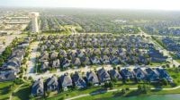 Serene retention lake mirrors blue sky behind waterfront homes in North Texas. High aerial perspective displays waterside residences, walking trails, distant horizon, Frisco, TX. USA
