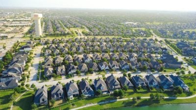 Serene retention lake mirrors blue sky behind waterfront homes in North Texas. High aerial perspective displays waterside residences, walking trails, distant horizon, Frisco, TX. USA