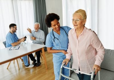 Doctor or nurse caregiver with senior woman using walker assistanece at home or nursing home