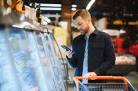 Young man buying groceries at the supermarket. Other customers in background. Consumerism concept