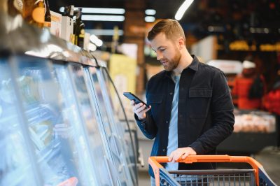 Young man buying groceries at the supermarket. Other customers in background. Consumerism concept