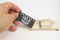A man pulls the bait from a mousetrap. Bait, a sheet of black paper with the inscription - yield trap. Finance and law concept.