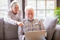 Happy white-haired 70-year-old couple at home using laptop together to shop online. Older people use new technologies