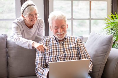 Happy white-haired 70-year-old couple at home using laptop together to shop online. Older people use new technologies