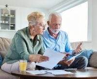 Senior couple checking bills and calculating expenses using a calculator at home, debt taxes and home budget concept, worried married elderly couple