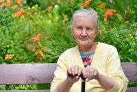 Portrait of an elderly woman, 80 years old, with a cane in her hands, relaxing on a bench in a park.