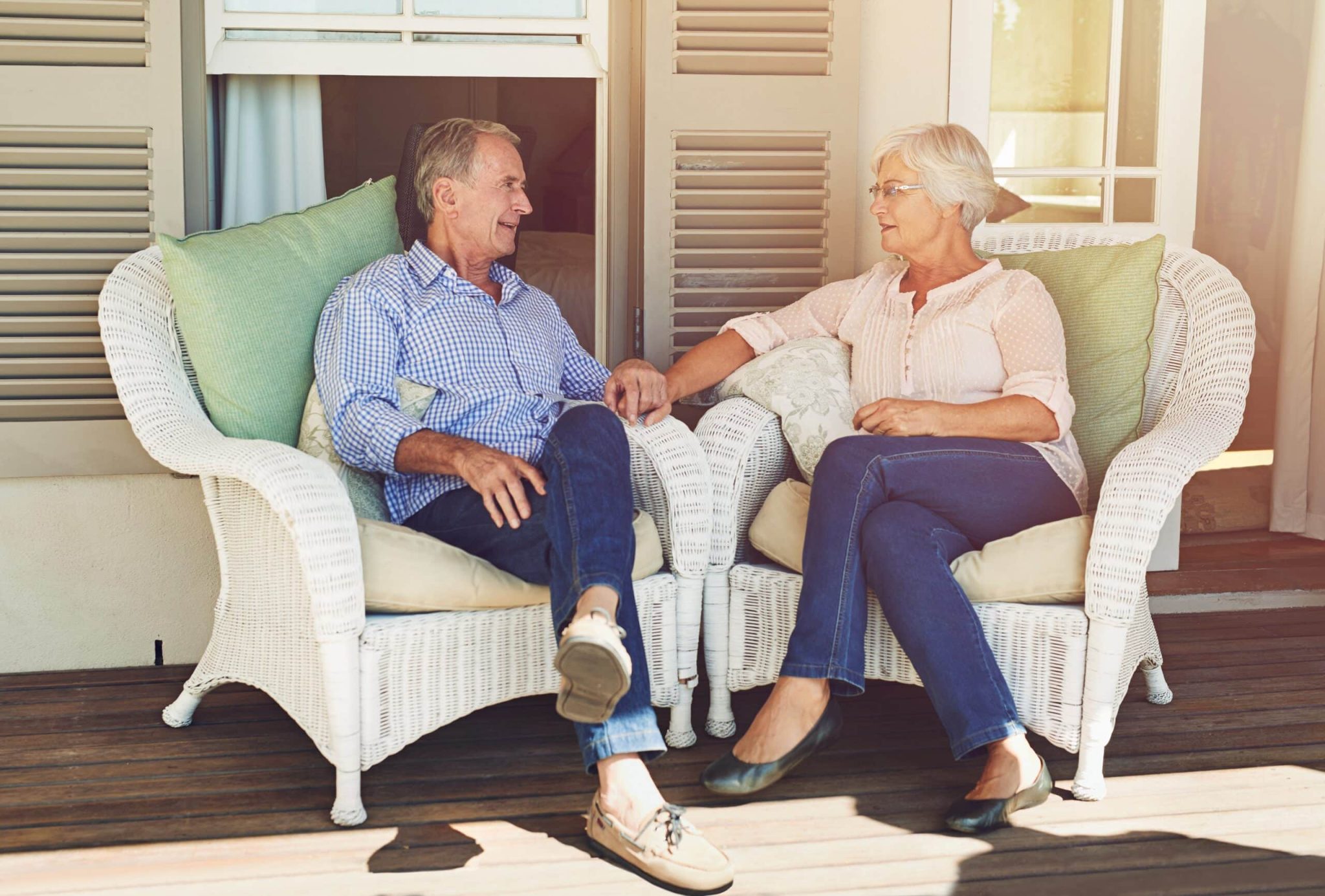 Elderly couple, holding hands and relax in home with love, bonding or trust on patio chairs. Marriage, senior people or support on porch with retirement comfort