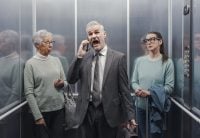 Stressed angry businessman shouting into his smartphone in the elevator, two women are annoyed and looking at each other