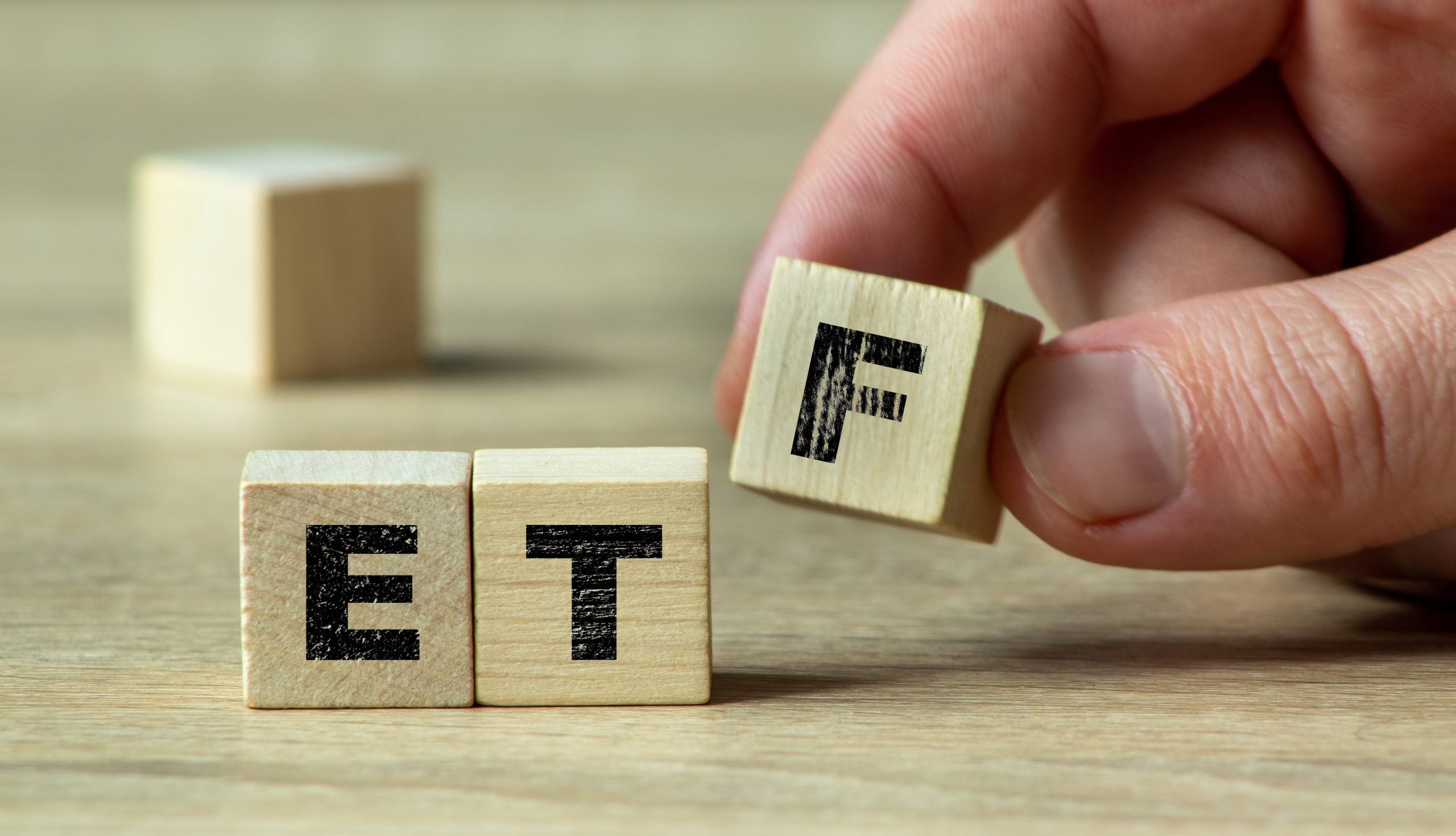 A hand arranging wooden blocks to form the acronym ETF on a light wooden surface. This image illustrates investment concepts, financial education, and stock market strategies.