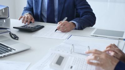 Close up of female accountant hands using calculator while collaborating with male colleague in office, calculating taxes and analyzing financial data. Audit and taxes in business