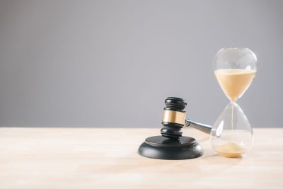 Hourglass, legal, law, time, court, justice, gavel, deadline concepts convey importance for lawyer judge decisions, sand flowing on wooden surface against grey background.