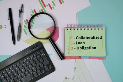 Finance and investment concept showing a CLO (Collateralized Loan Obligation) notepad surrounded by stock charts, magnifying glass, keyboard and pens to represent analysis and risk assessment.