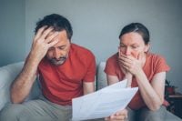 Worried middle-aged couple reviewing bills and financial documents at home, stress and concern, selective focus