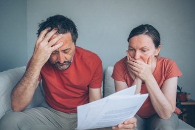 Worried middle-aged couple reviewing bills and financial documents at home, stress and concern, selective focus
