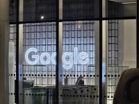 Large illuminated Google logo behind the glass facade of an office building at night
