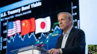 A man with gray hair, Ray Dalio, stands behind a transparent podium speaking into two microphones. He wears a dark suit jacket over a light striped shirt. Behind him, a large dark screen displays "U.S. Treasury Bond Yields" in white text. Below the text are the flags of the United States, China, and Japan, arranged horizontally, positioned above a blue and green line graph. In the bottom right corner of the image, the '24/7 WALL ST' logo is visible.