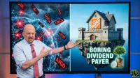 A man with a beard and a light blue shirt, Jim Cramer, stands in front of a large screen. The screen is split into two halves. The left half shows a dark, stormy, digital network with glowing red points and red floating text boxes for stock tickers like AI, NVDA, ORCL, and AVGO. The right half displays a bright blue sky above a floating rock island, on which sits a castle-like house with 'THE HOME DEPOT' logo. Below the house, text reads 'BORING DIVIDEND PAYER', next to a stack of gold coins and a small green tree.