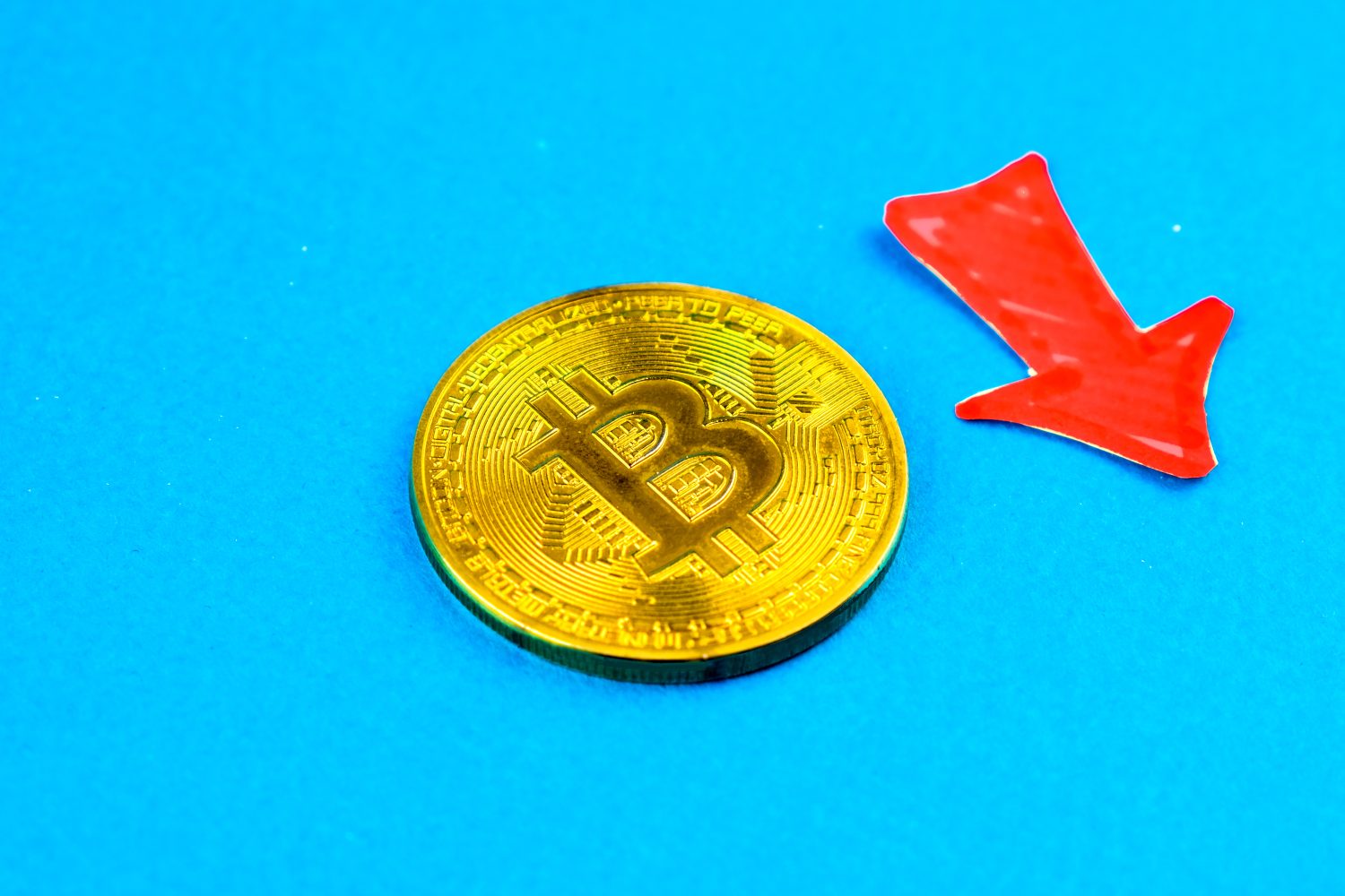 Bitcoin on blue background with red arrow. Concept of bitcoin falling further below.