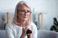 Sad lonely thoughtful pensive old mature woman hold cane stick sit alone on sofa, upset poor depressed senior retired grandma having health problem think of loneliness disease in retirement house
