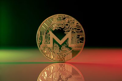 Monero XMR cryptocurrency physical coin placed on reflective surface and lit with green and red lights