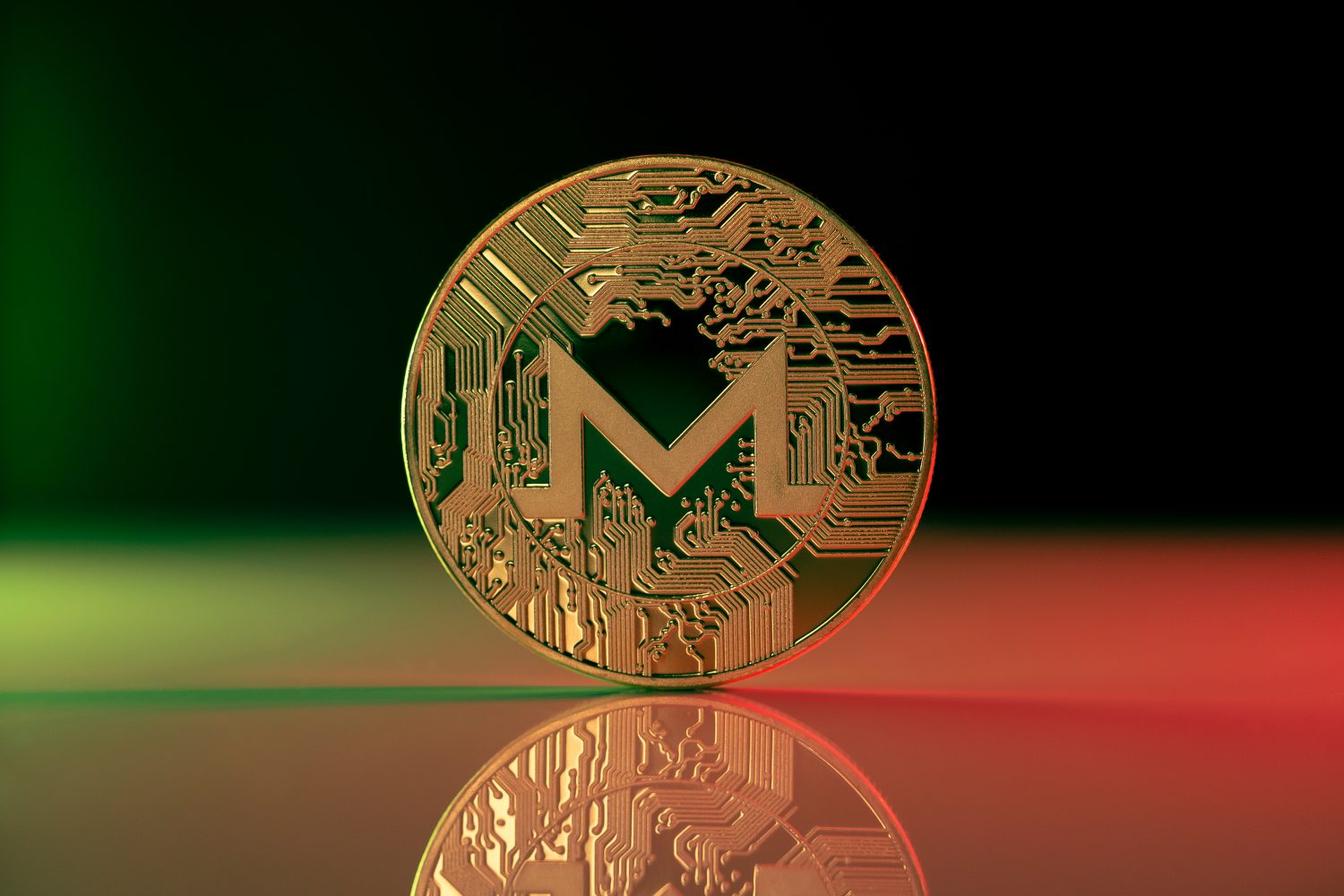 Monero XMR cryptocurrency physical coin placed on reflective surface and lit with green and red lights