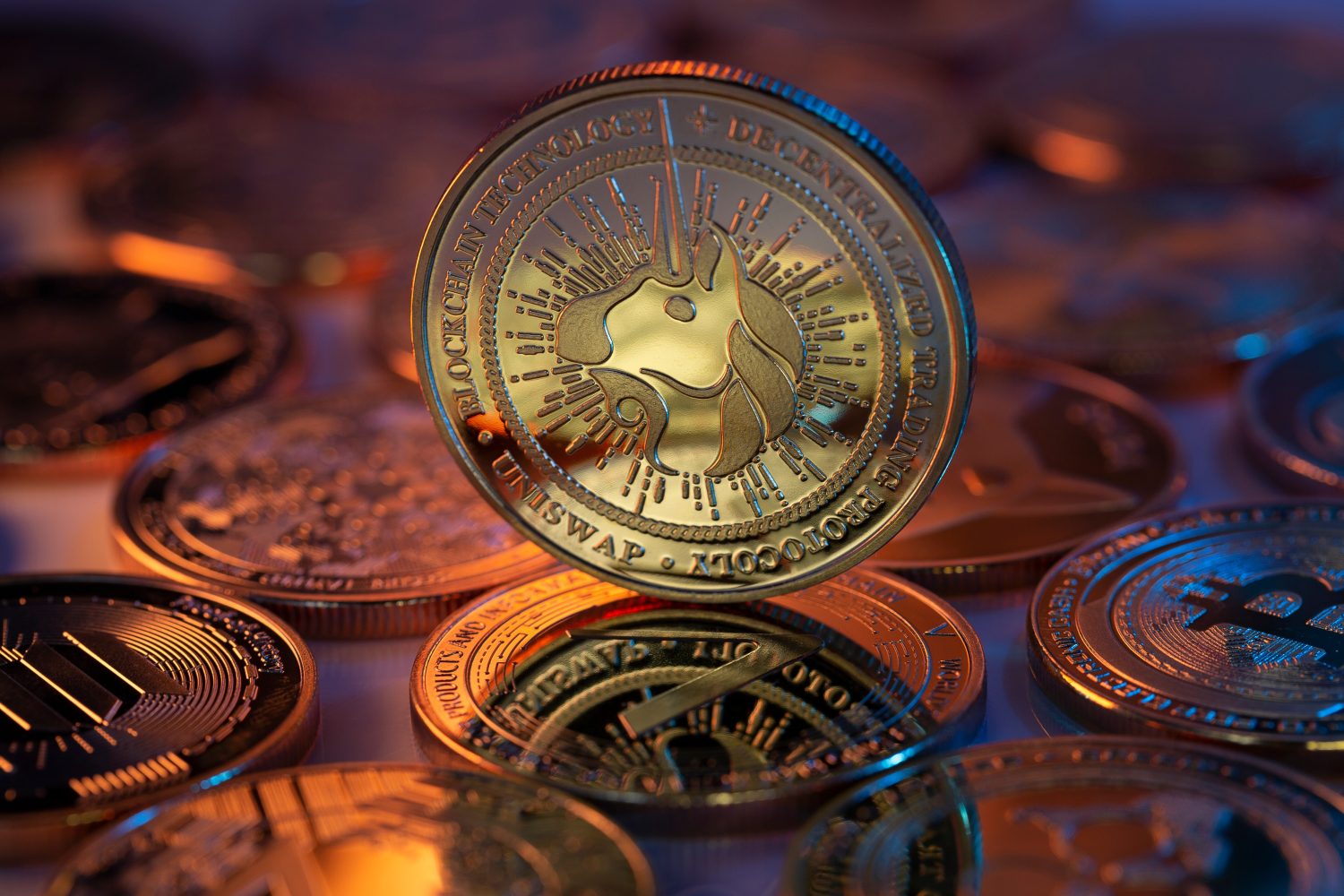 Uniswap UNI Cryptocurrency Physical Coin placed on crypto altcoins and lit with orange and blue lights. Macro shot. Selective focus.