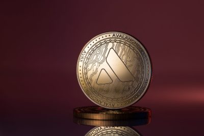Avalanche AVAX Cryptocurrency Physical Coin Placed on reflective surface and lit with red and purple lights.
