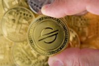 Cryptocurrency concept. two male fingers holding a shiny STELLAR cryptocurrency coin in top of piles of different cryptocurrency coins . selective focus.