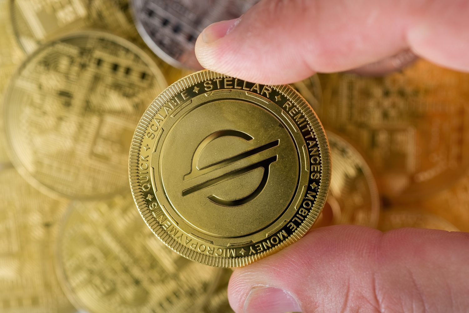 Cryptocurrency concept. two male fingers holding a shiny STELLAR cryptocurrency coin in top of piles of different cryptocurrency coins . selective focus.