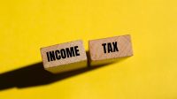Income tax message written on wooden blocks with yellow background. Conceptual income tax symbol. Copy space.