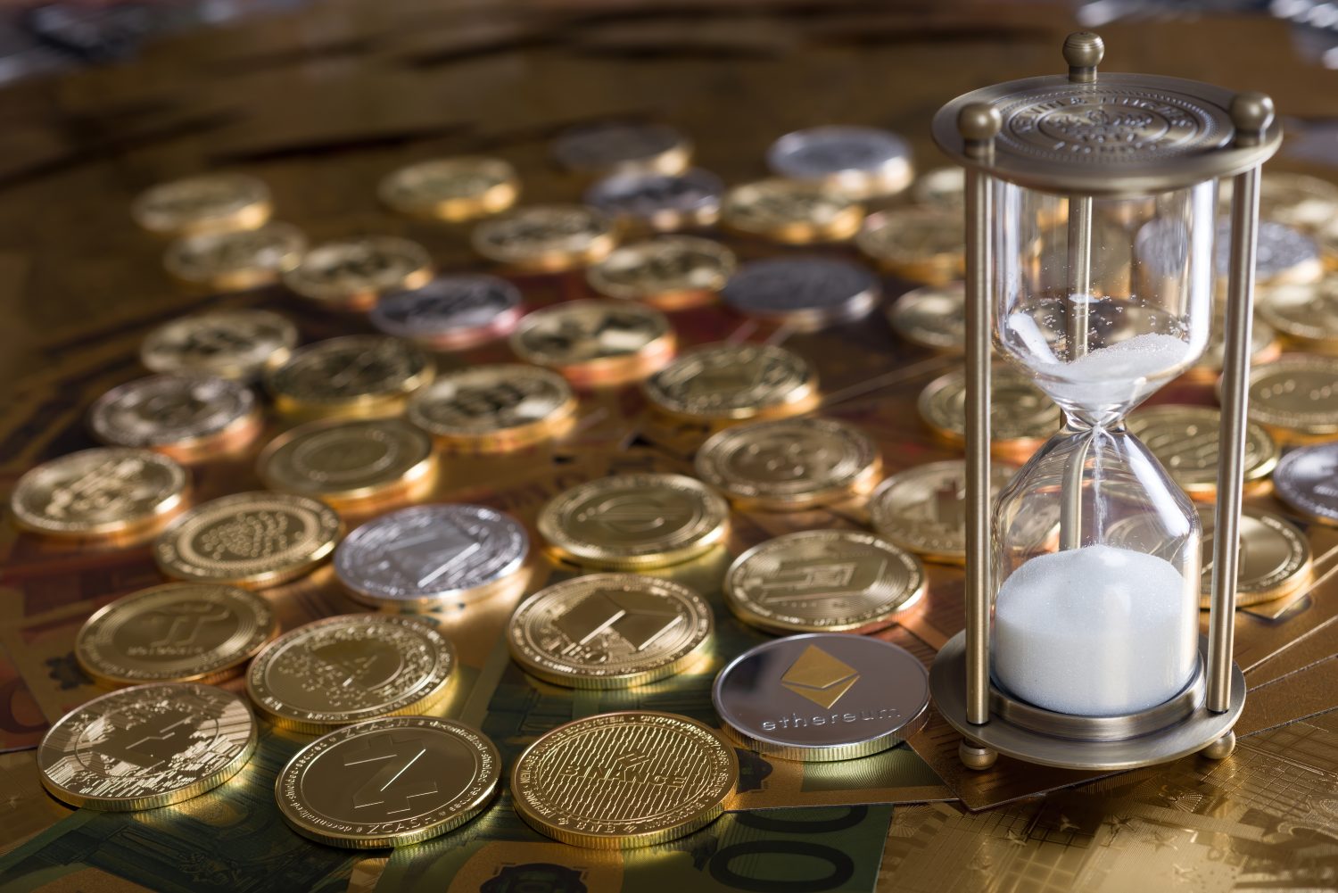 Cryptocurrency concept. A pile of cryptocurrency coins by an hourglass in top of the seven different denominations of euro banknotes €5, €10, €20, €50, €100, €200, and €500. selective focus.