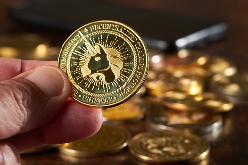 A person holds a Uniswap token over a wooden surface, surrounded by other coins. Several tokens are scattered nearby, showcasing the growing interest in digital assets.