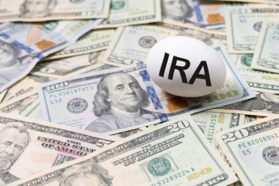 Financial planning for retirement featuring a white egg labeled Individual Retirement Account, IRA placed on a bed of U.S. dollar bills, represented by the nest egg metaphor.
