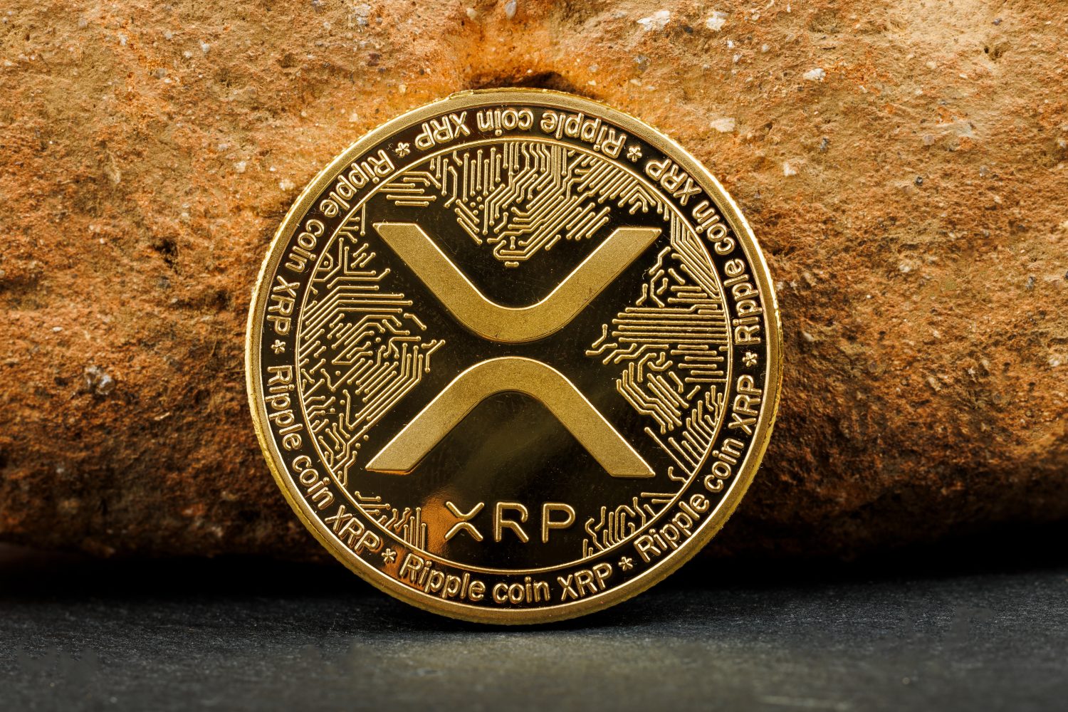 Ripple XRP cryptocurrency coin with golden details placed against a textured rock background.