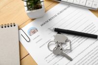 Blank house rental agreement with key on wooden background, closeup