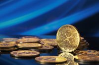 A collection of golden Xrp cryptocurrencies lies spread out on a shiny surface. The backdrop features a vibrant blue digital pattern, emphasizing the cryptocurrency theme.